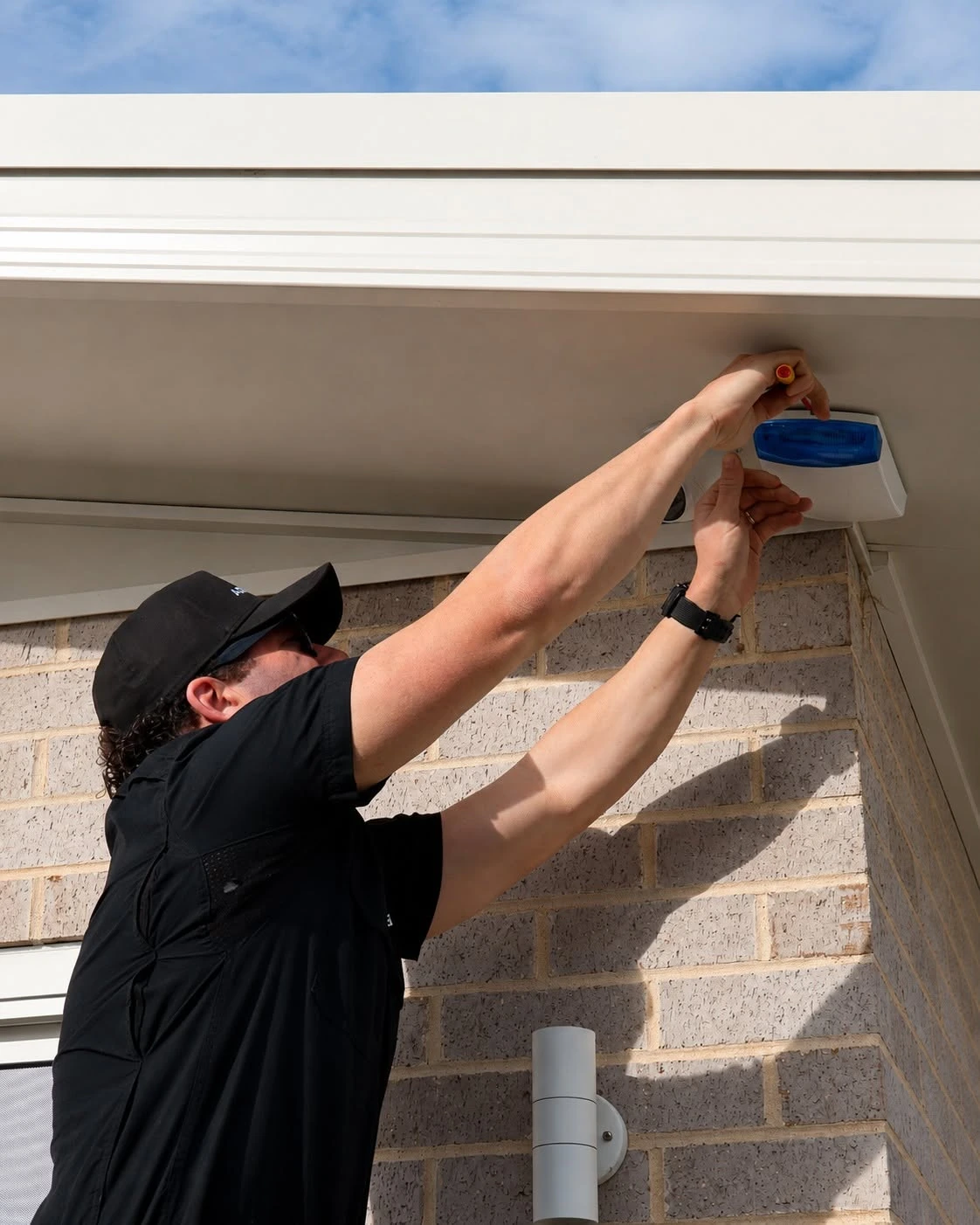 An Armitage Security technician fitting an external alarm siren and strobe under the eave of a Nowra home