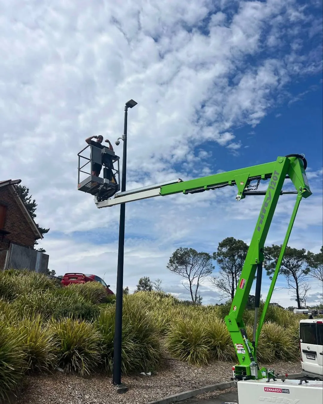 An Armitage Security technician in a boom lift fitting a camera to a tall light pole at a commercial site