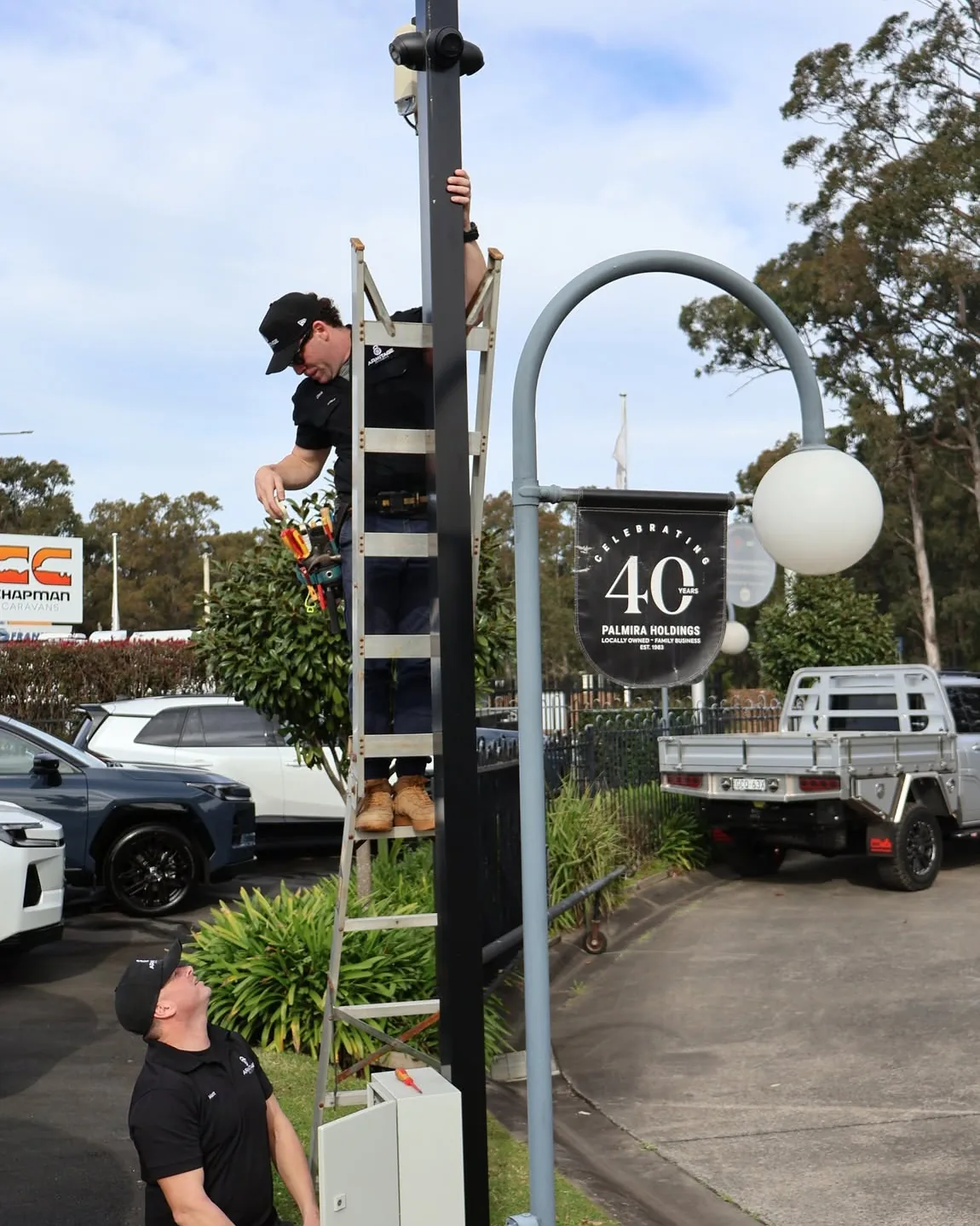 Two Armitage Security technicians fitting a camera to a signage pole at a Nowra car dealership