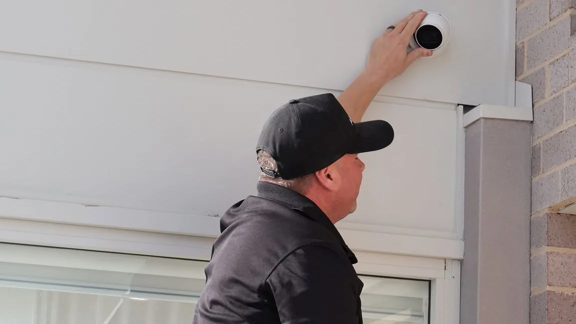 An Armitage Security technician fitting a turret camera under the eaves of a Shoalhaven home