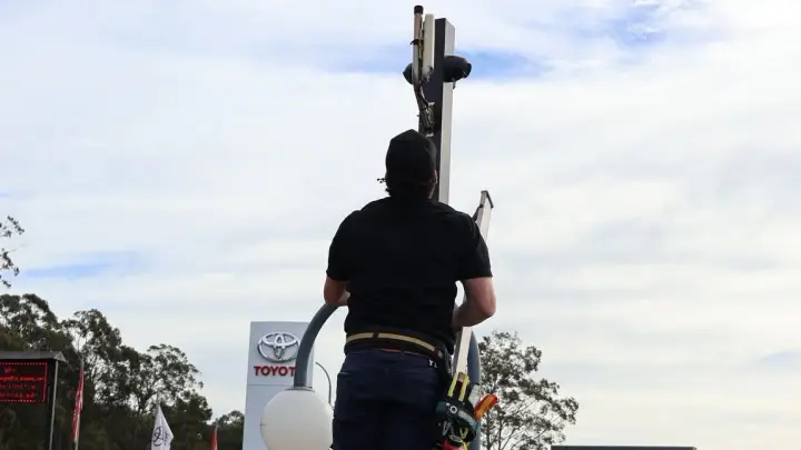 An Armitage Security technician on a ladder fitting a pole camera at a Nowra car dealership