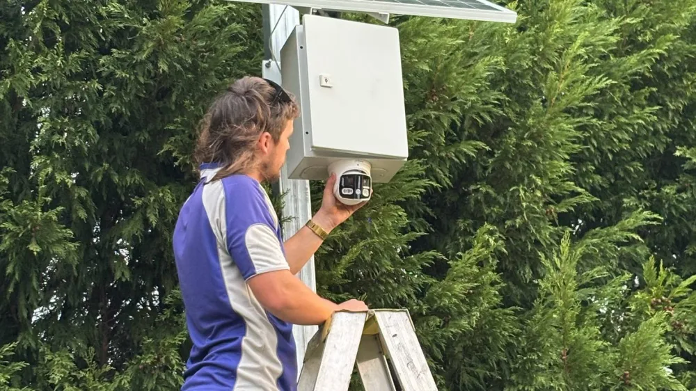 An Armitage Security technician on a ladder fitting a solar powered camera in a hedge