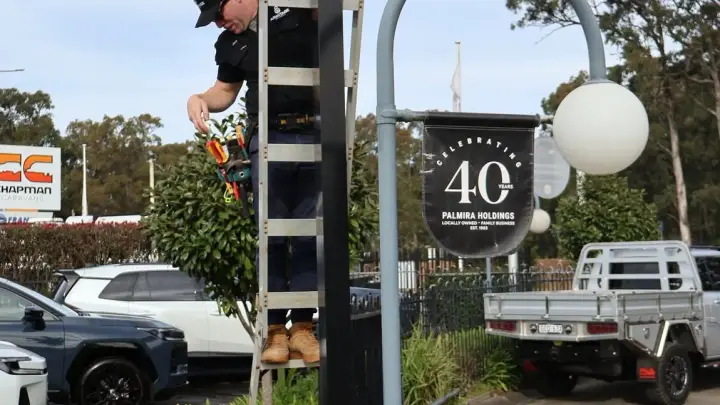 Two Armitage Security technicians fitting a camera to a signage pole at a Nowra car dealership